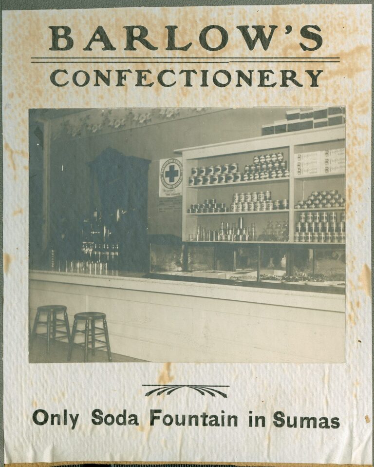 Interior of an 1891 Sumas confectionery with a soda fountain, wooden stools, and candy display cases