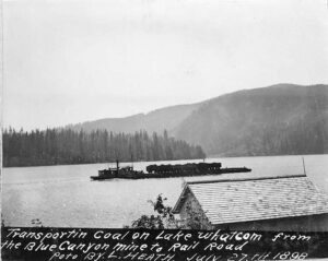 1898 photograph of a tug and coal barge on Lake Whatcom with forested shoreline