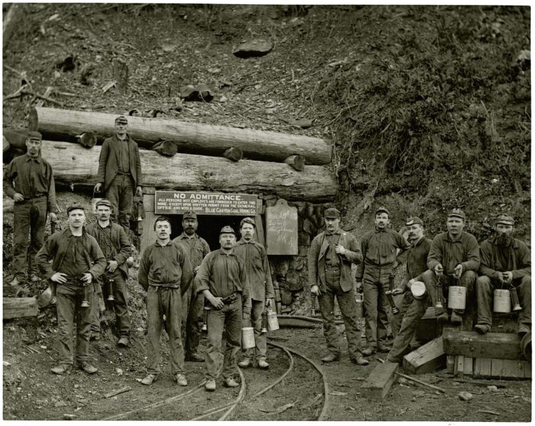 Group of thirteen coal miners at the timber-framed entrance of a mine