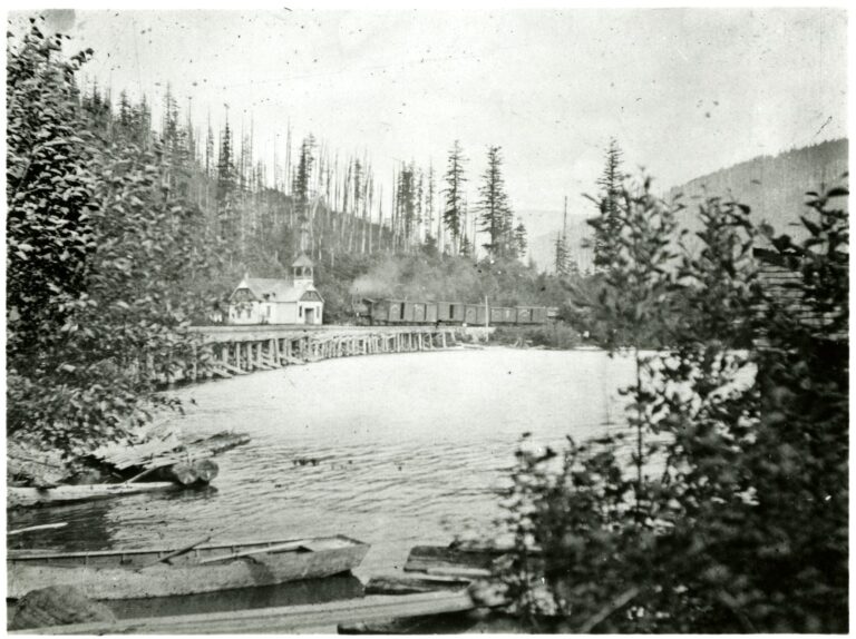 Black and white photo of the Blue Canyon schoolhouse beside a railway trestle on Lake Whatcom