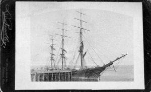Three-masted sailing ship tied up at a wooden dock in early Fairhaven