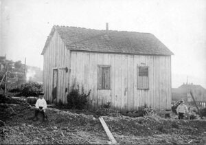 Sepia around-1891 photo of the first wooden schoolhouse on Bellingham Bay