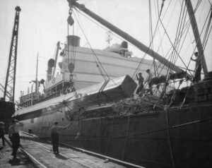 Workers loading stacks of lumber onto a cargo ship at a mill dock