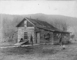A woman seated on a log-house cellar door beside two men, Whatcom County, 1870s