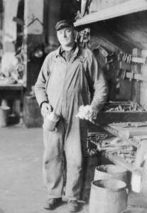 Sawmill worker holding an oil can and machine parts, about 1922
