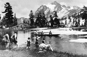 Around 1927 photograph of tourists swimming and boating on a lake beside Mt. Baker Lodge at Heather Meadows